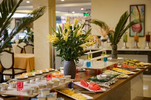 A buffet setup with various food items and a centerpiece of yellow flowers. - Freesia Hotel (Sa Pa)