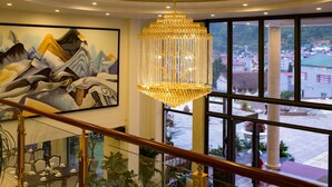 A grand chandelier, a mural, and a view of the city through large windows. - Freesia Hotel (Sa Pa)