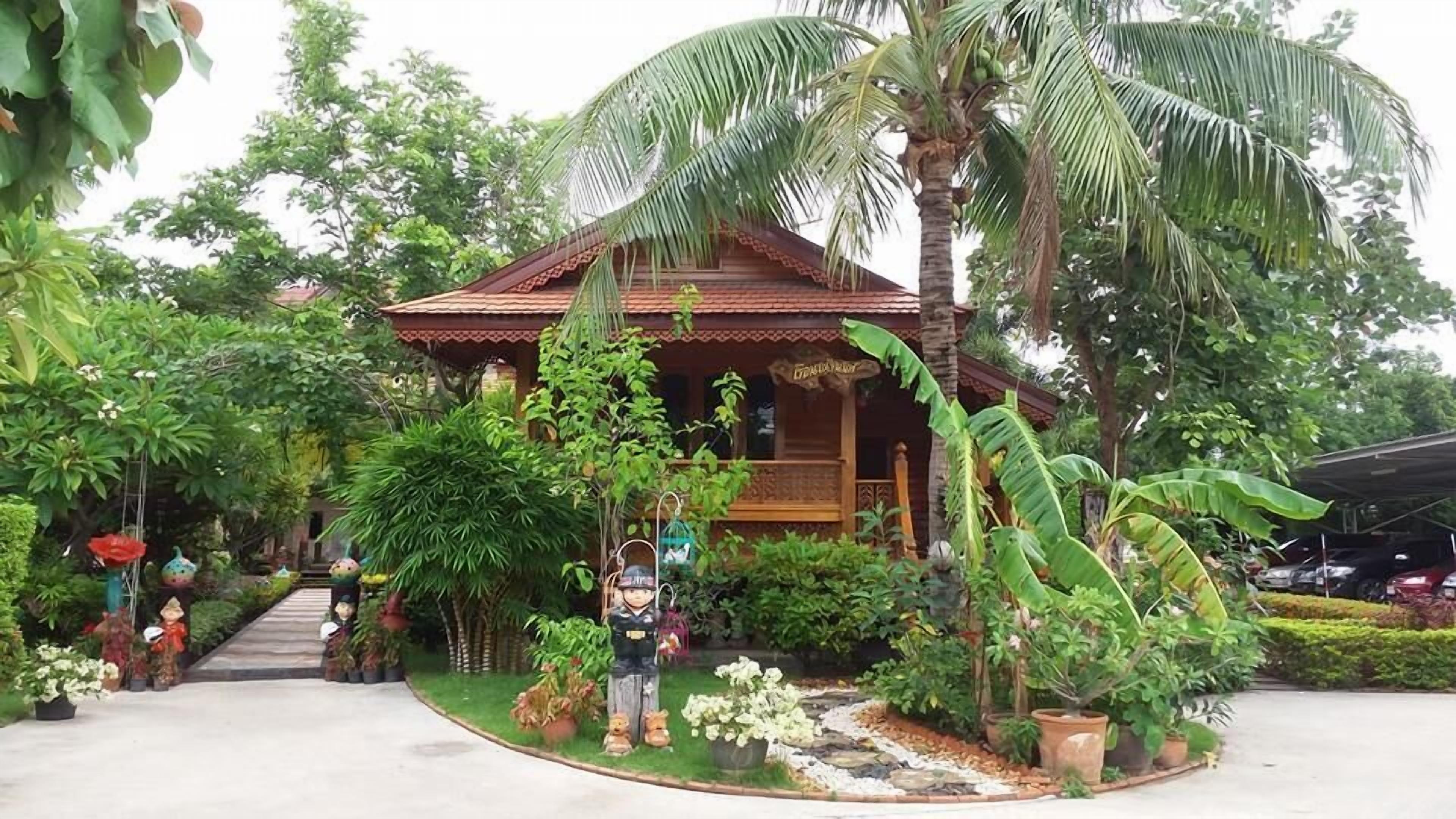 A traditional wooden house surrounded by lush greenery, including palm trees and various plants.