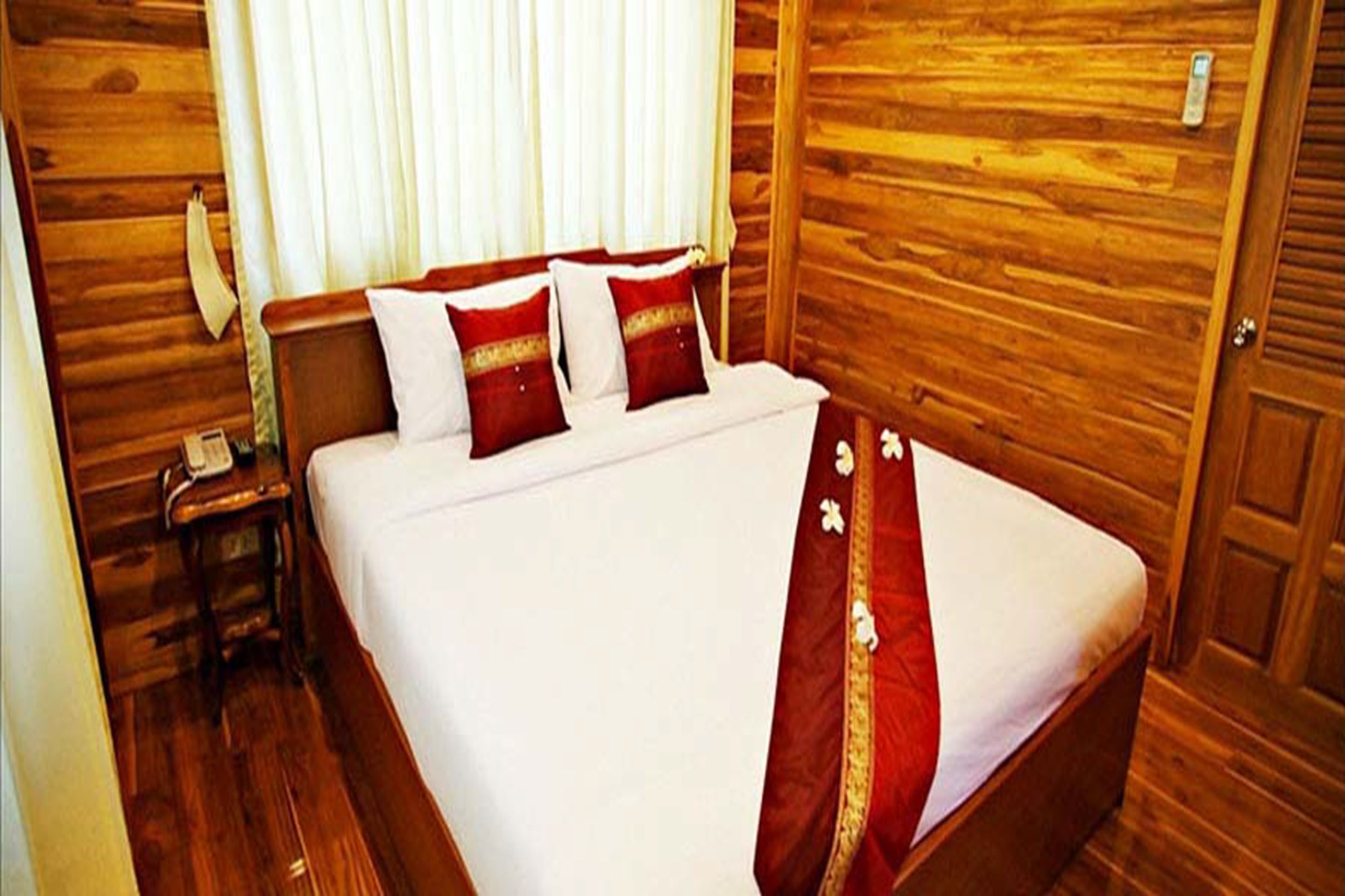 A wooden-paneled room with a bed, a nightstand, and a telephone.