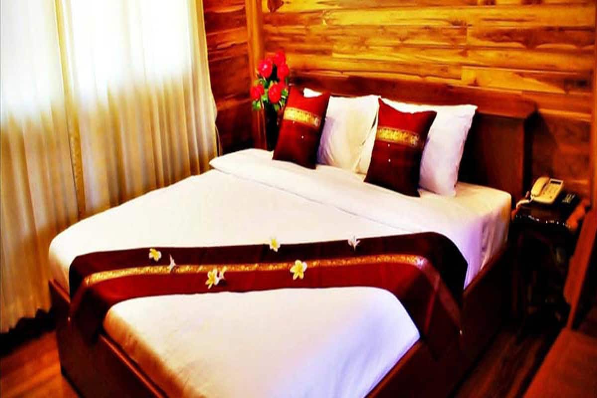 Un grand lit avec du linge de lit blanc et des oreillers rouges et blancs, une tête de lit en bois et une table de chevet avec un téléphone.