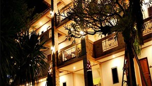 Un edificio de varios pisos con balcones, iluminación exterior y plantas.