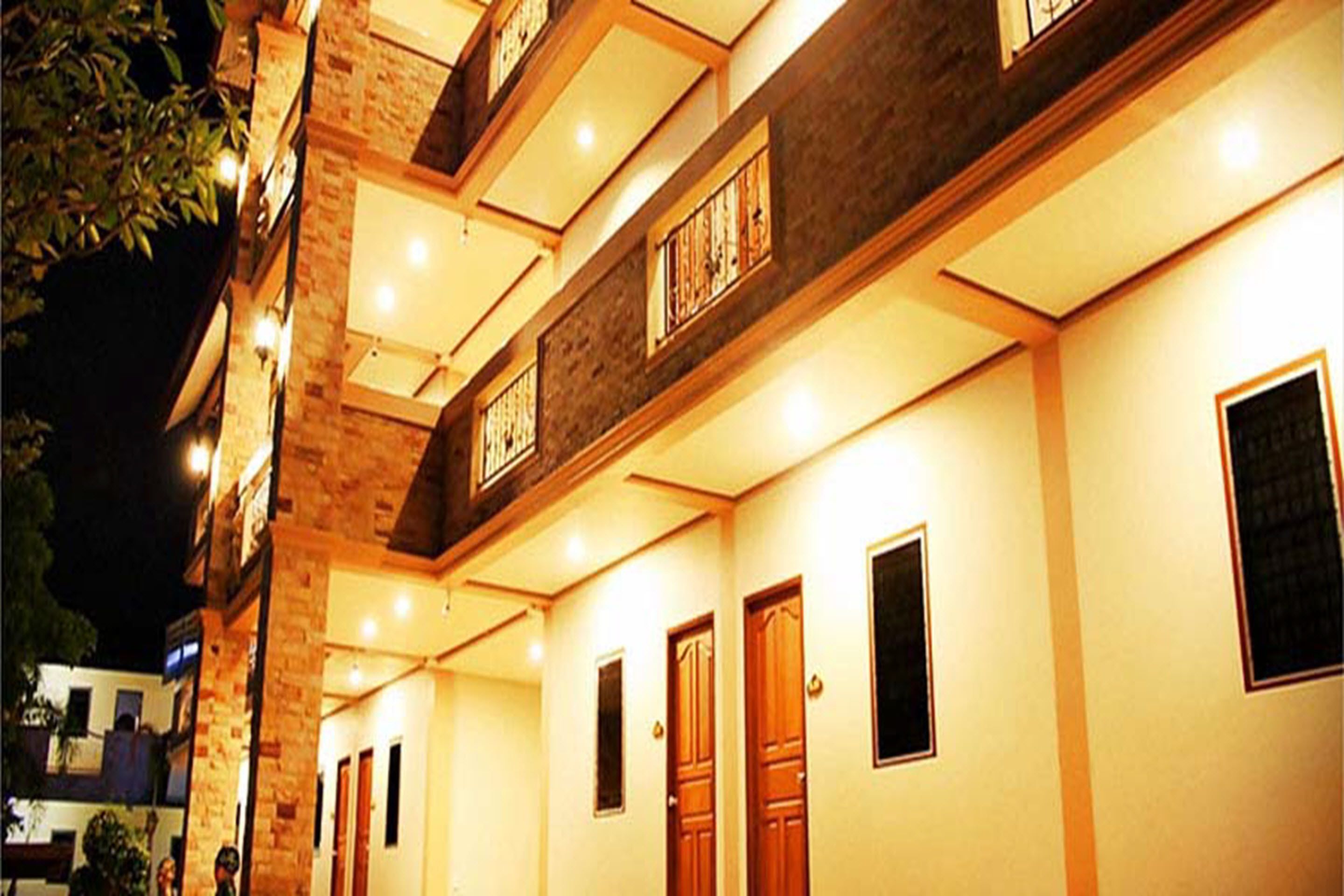 Un hotel de varios pisos con fachada de ladrillo, múltiples balcones y una serie de puertas que dan a habitaciones individuales.