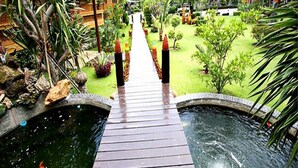 Un sendero de madera que lleva a una piscina, flanqueada por un jardín tropical.