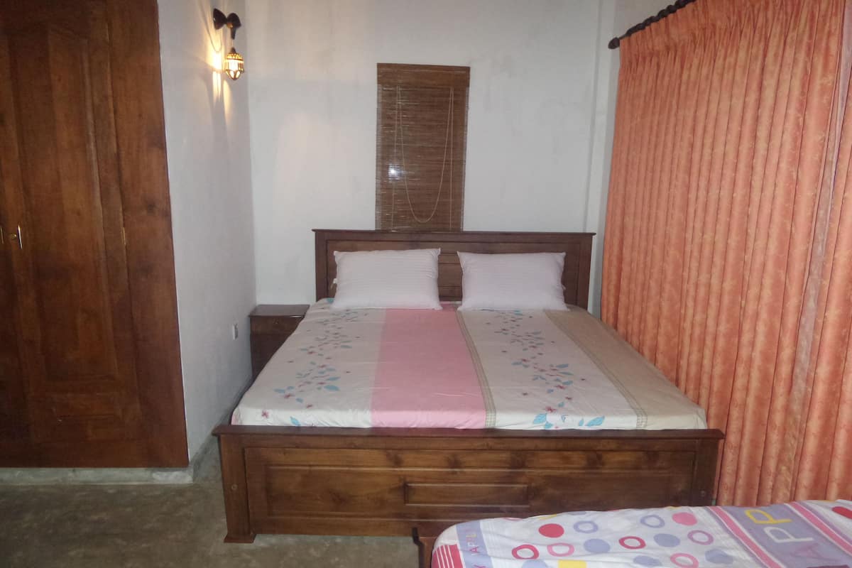 A bedroom with a wooden bed, a nightstand, a wardrobe, and a window with blinds.