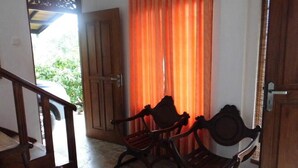 A room with a wooden staircase, two wooden rocking chairs, and a door with orange curtains. - CoCoWorld Bungalow (Panduwasnuwara)