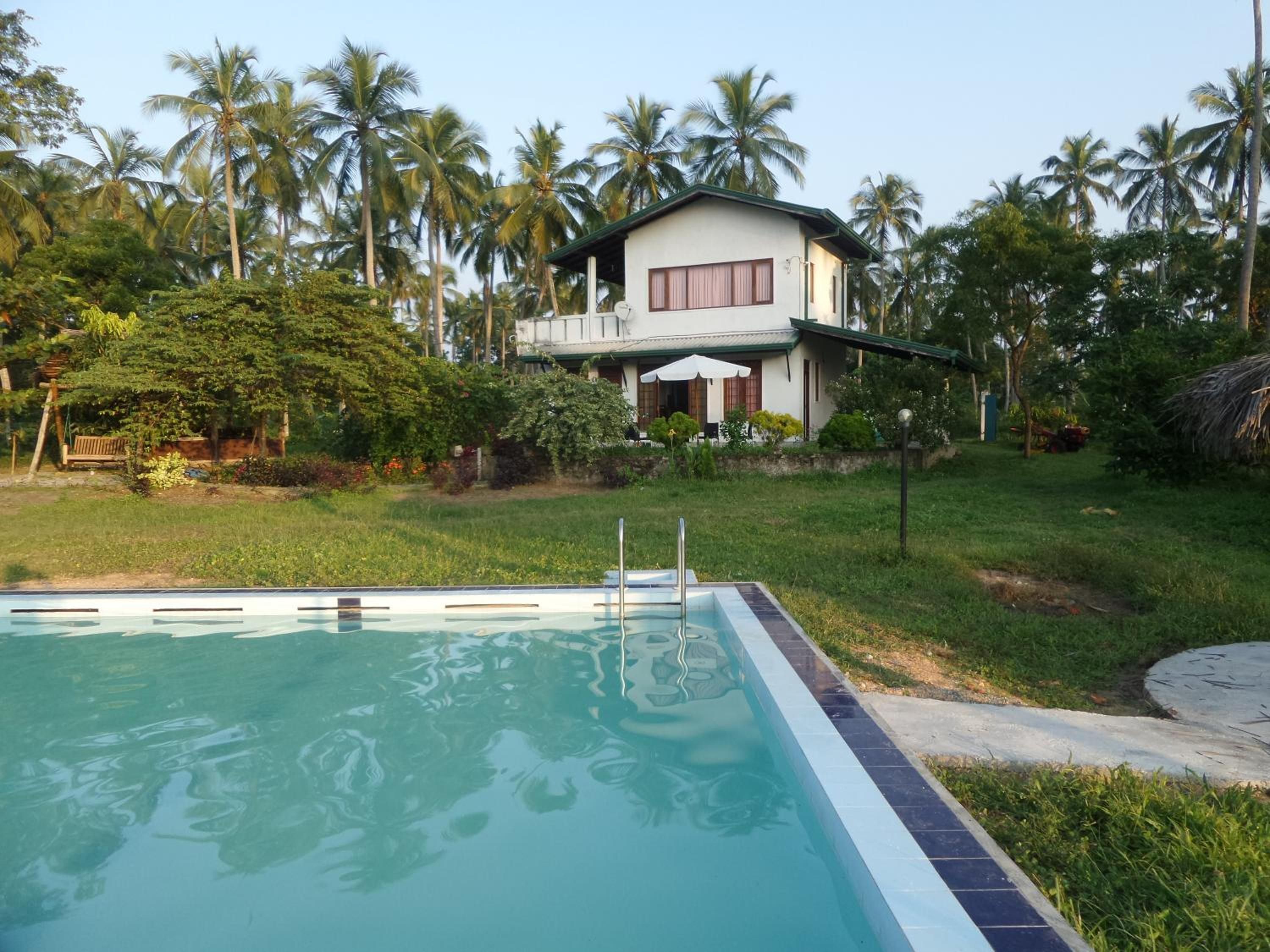 Ein Schwimmbecken mit glasklarer Wasserfläche, umgeben von einem gepflegten Rasen und einem Haus mit Balkon.