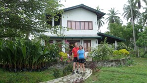 A house with a garden pathway leading to it, surrounded by lush greenery and palm trees. - CoCoWorld Bungalow (Panduwasnuwara)