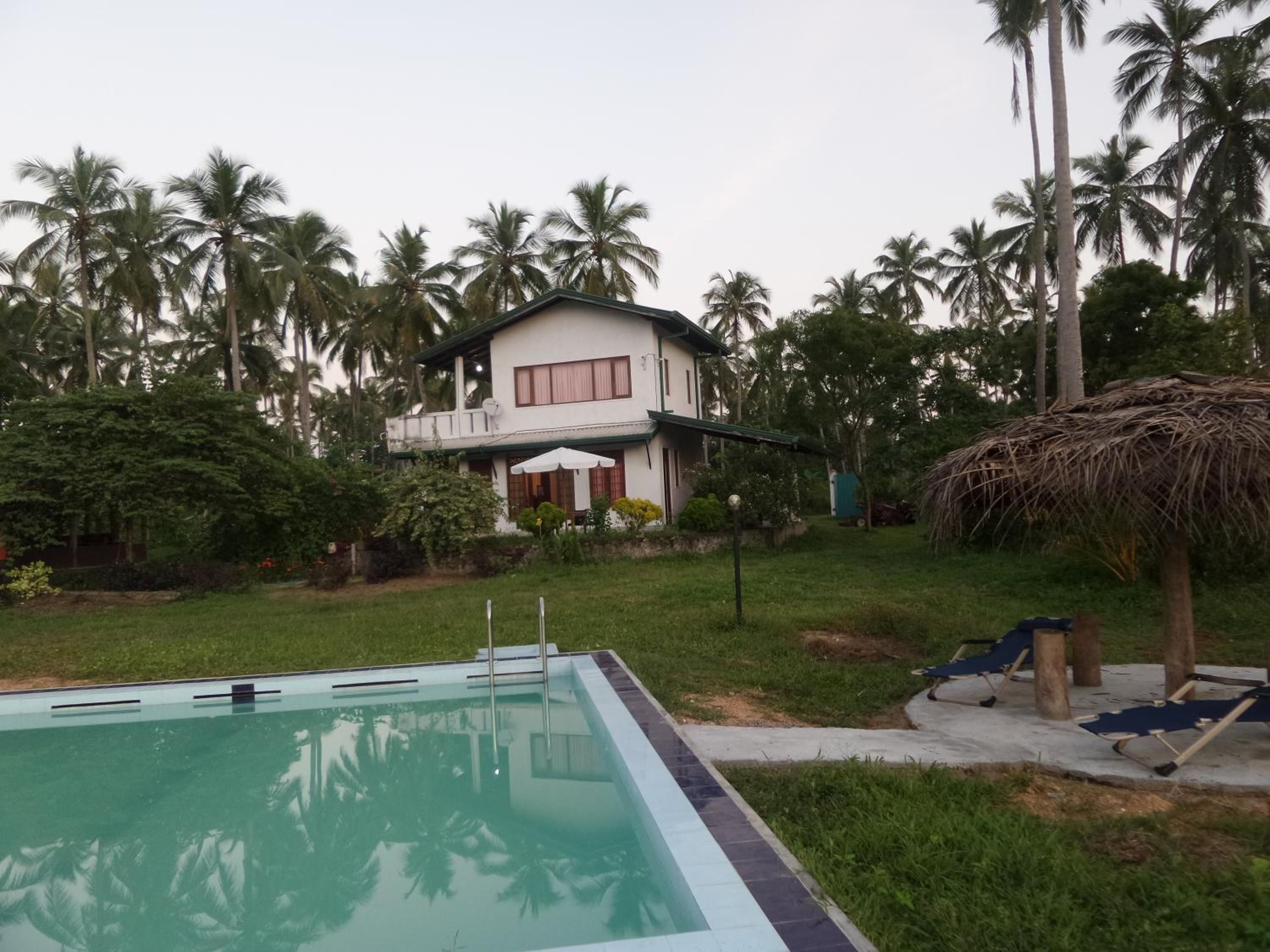 Una casa de dos pisos con piscina, rodeada de palmeras.