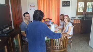 A family dining at a wooden table in a room with a kitchen and a TV.