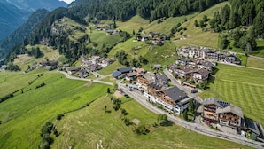 Vista aèria d'un poble de muntanya amb cases tradicionals d'estil chalets, una carretera principal i turons verds al voltant.