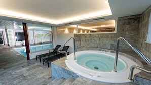 Zona d'una piscina interior moderna, amb un bany d'hidromassatge, gandules i un paviment de pedra.