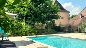 Una piscina con borde de baldosas, rodeada de follaje y una valla de madera.