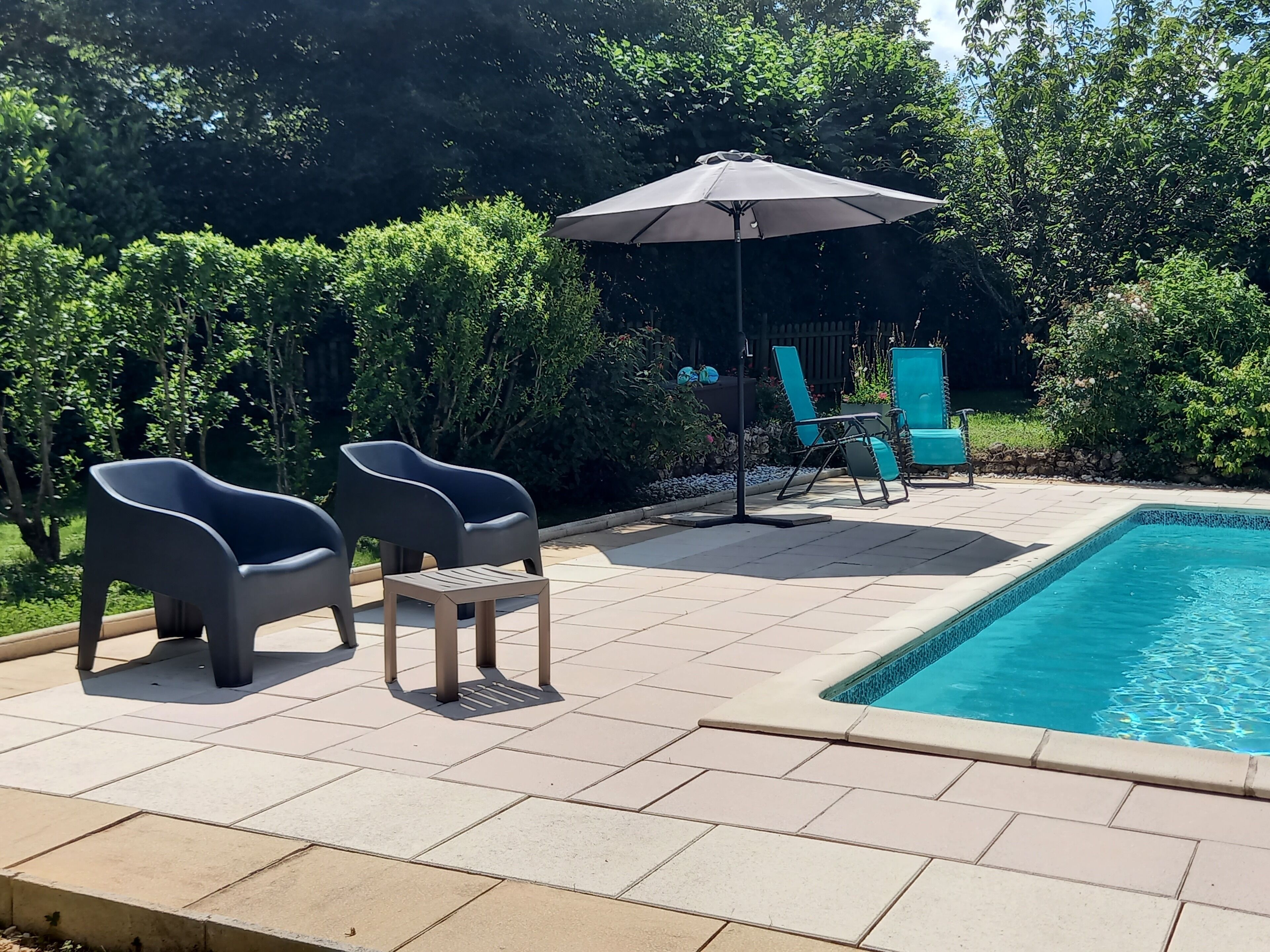A pool area with two lounge chairs, a small table, and a patio umbrella.