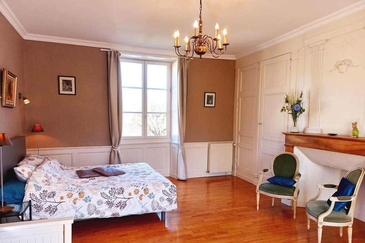 Une chambre à coucher comprenant un lit, une chaise, une commode, une fenêtre et un lustre.