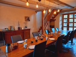 A dining area with a wooden table set for six, surrounded by chairs. A wooden cabinet with decorative items is to the left.