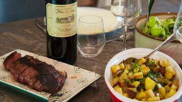 A dining table with a bottle of wine, a plate of steak, a bowl of potatoes, and a glass of water.