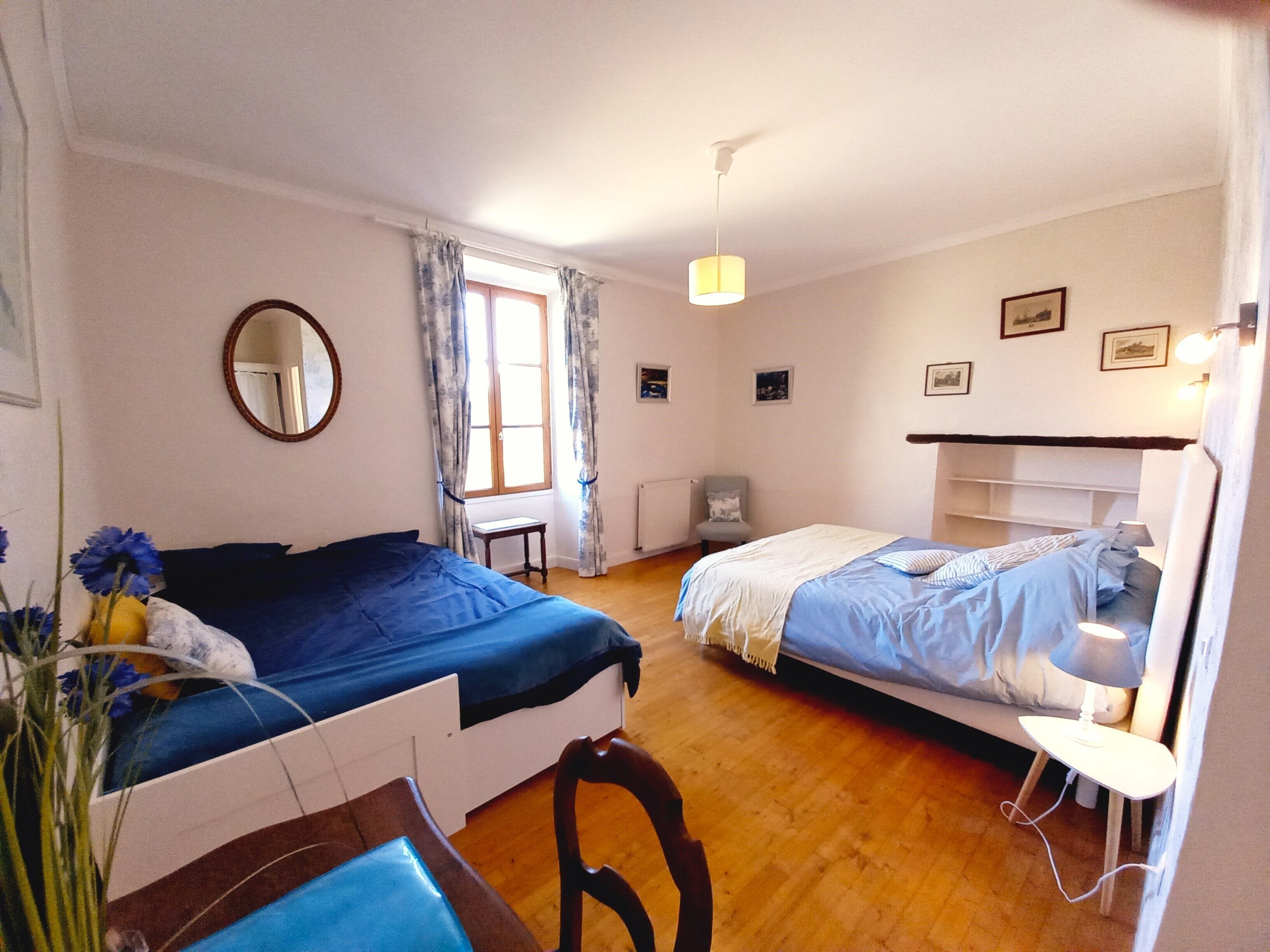 Un dormitorio con dos camas, un espejo, una ventana con cortinas y una mesita de noche con lámpara.