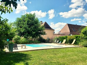 Una piscina con sillas de descanso, un césped y un edificio con techo inclinado.
