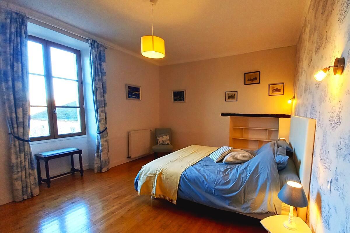 Une chambre à coucher comprenant un lit, une table de chevet, une chaise, une fenêtre avec des rideaux et des lampes fixées au mur.