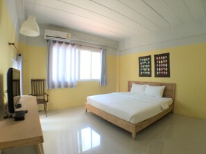 Un dormitorio con cama, escritorio, silla, aire acondicionado y ventana con cortinas.