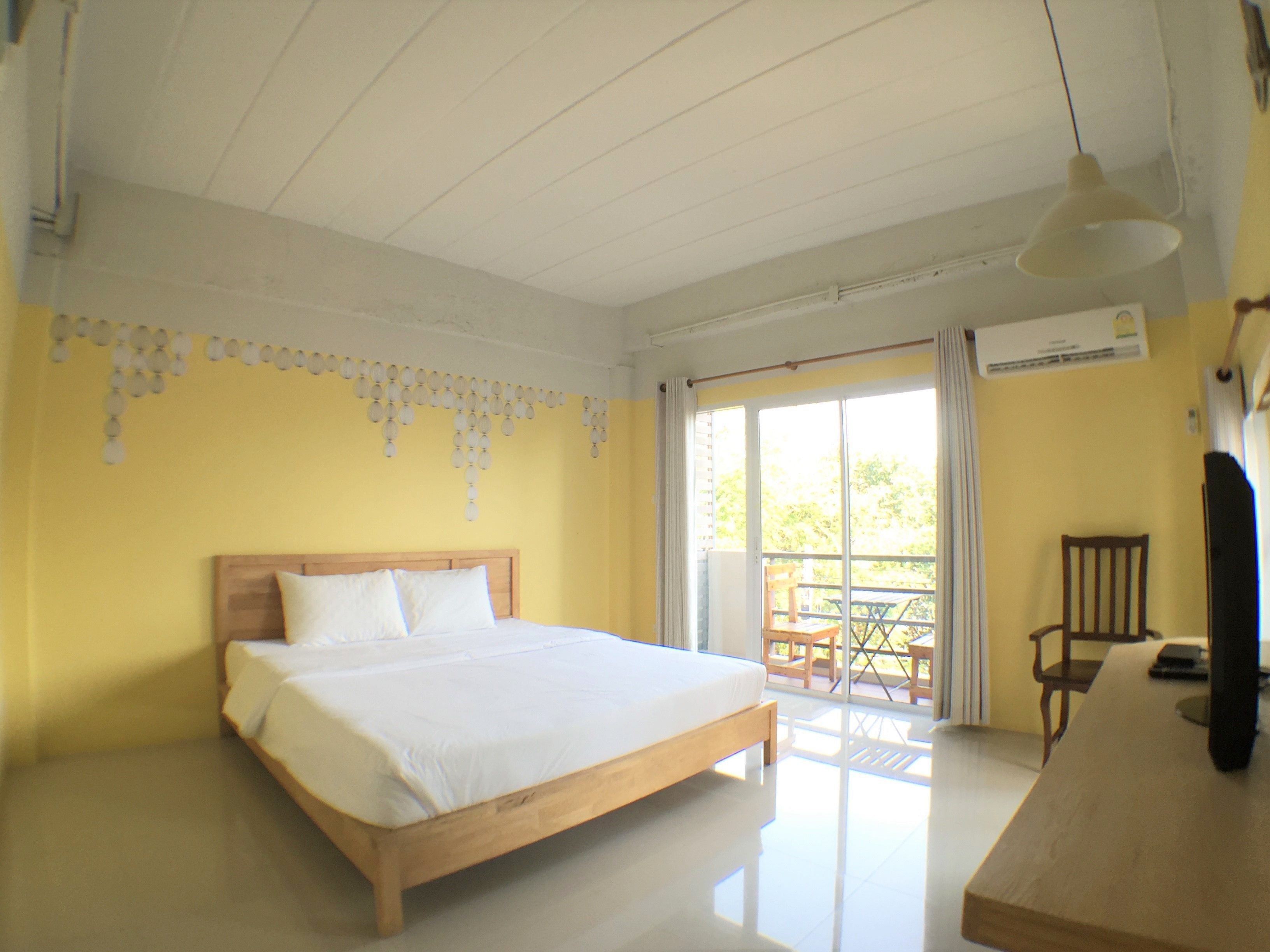A bedroom with a wooden bed, a balcony with a table and chairs, and a ceiling fan.