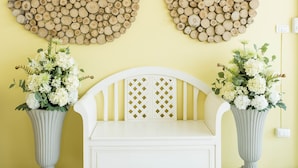 Ein Zimmer mit einer weißen Bank, zwei Vasen mit Blumen, einer geometrischen Leuchte und einer Wand, die mit Holzstämmen verziert ist.