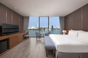 A modern hotel room with a large bed, a TV, a desk, and a view of the city skyline. - Avora Hotel (Da Nang)