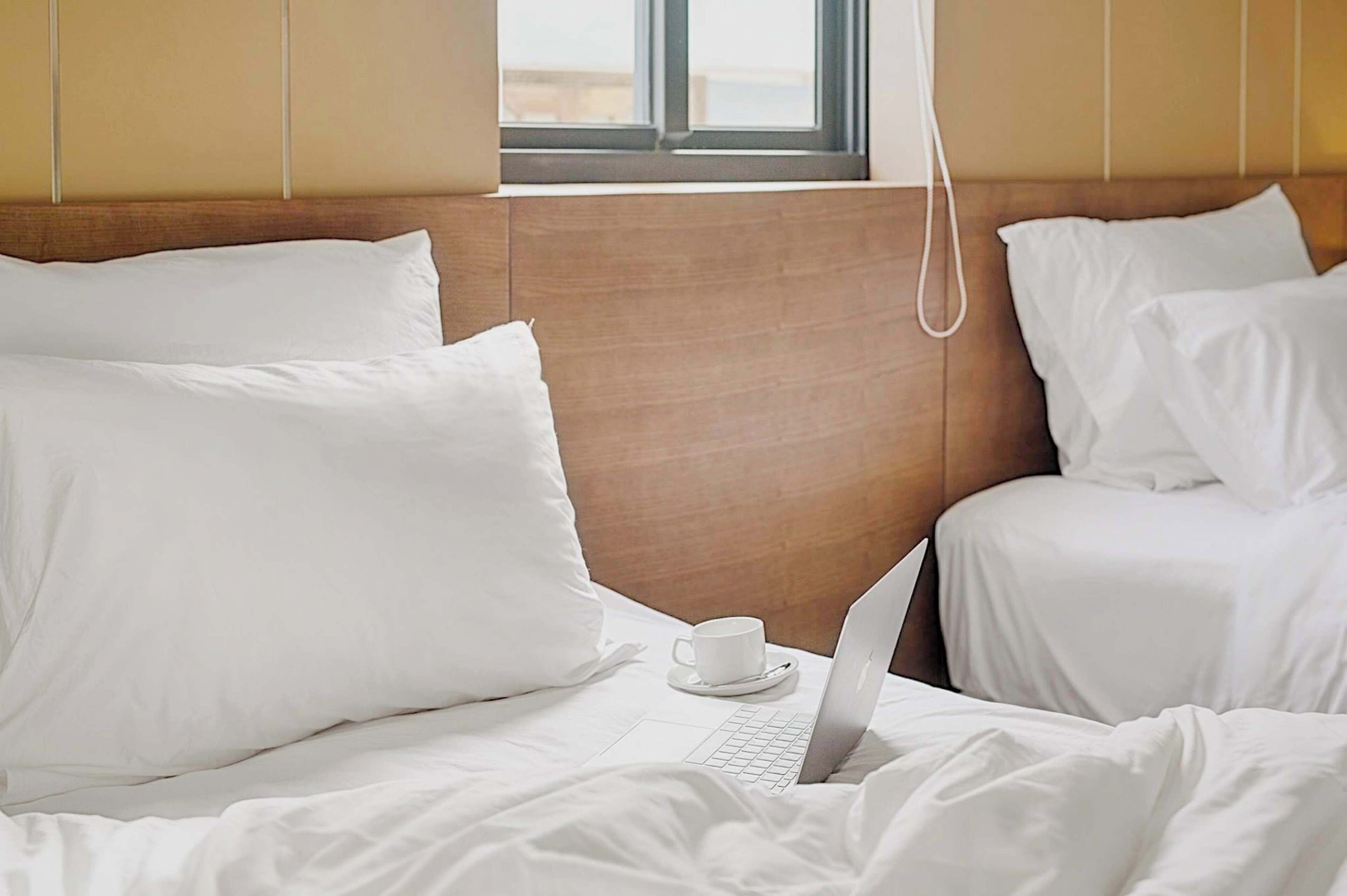 Une chambre d’hôtel avec un lit, un ordinateur portable et une tasse posée sur le lit.