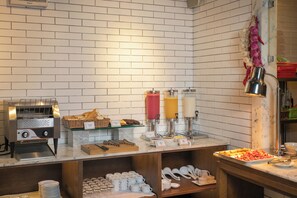 Un bufé de desayuno con una máquina de café, dispensadores de zumo y una variedad de alimentos.