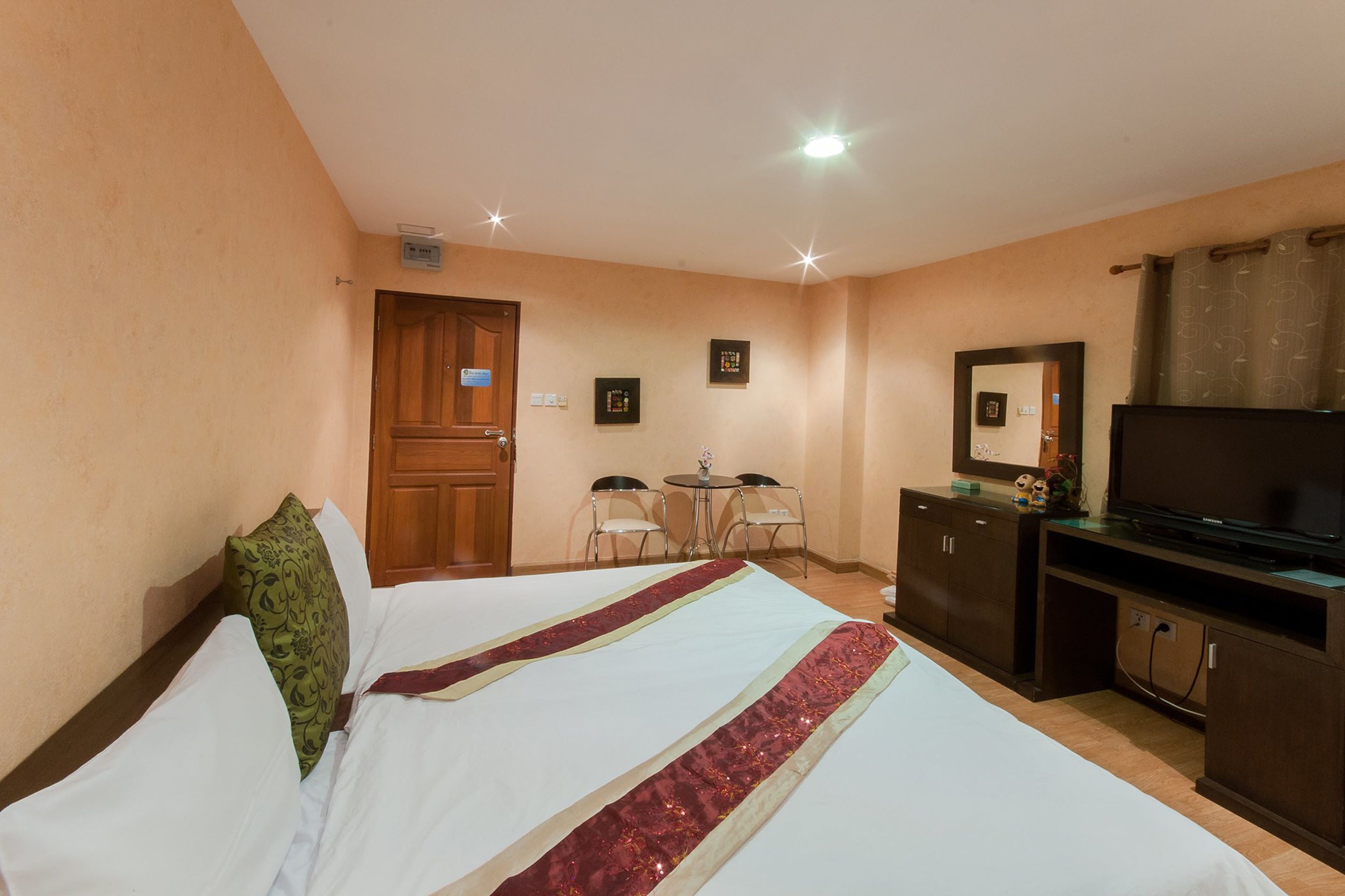 Una habitación de hotel con una cama, un escritorio con sillas, un televisor y un espejo.