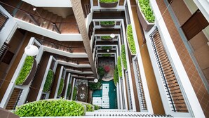 A multi-level atrium with a central staircase, green planters, and a patterned floor. - Sa-Bai-Dee Condo (Chonburi)