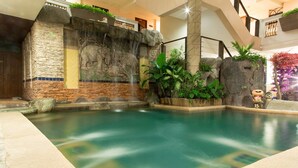 A pool area with a waterfall and stone walls, surrounded by plants and a decorative tree. - Sa-Bai-Dee Condo (Chonburi)