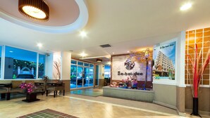 A hotel lobby with a reception desk, seating area, and a large window overlooking the street. - Sa-Bai-Dee Condo (Chonburi)