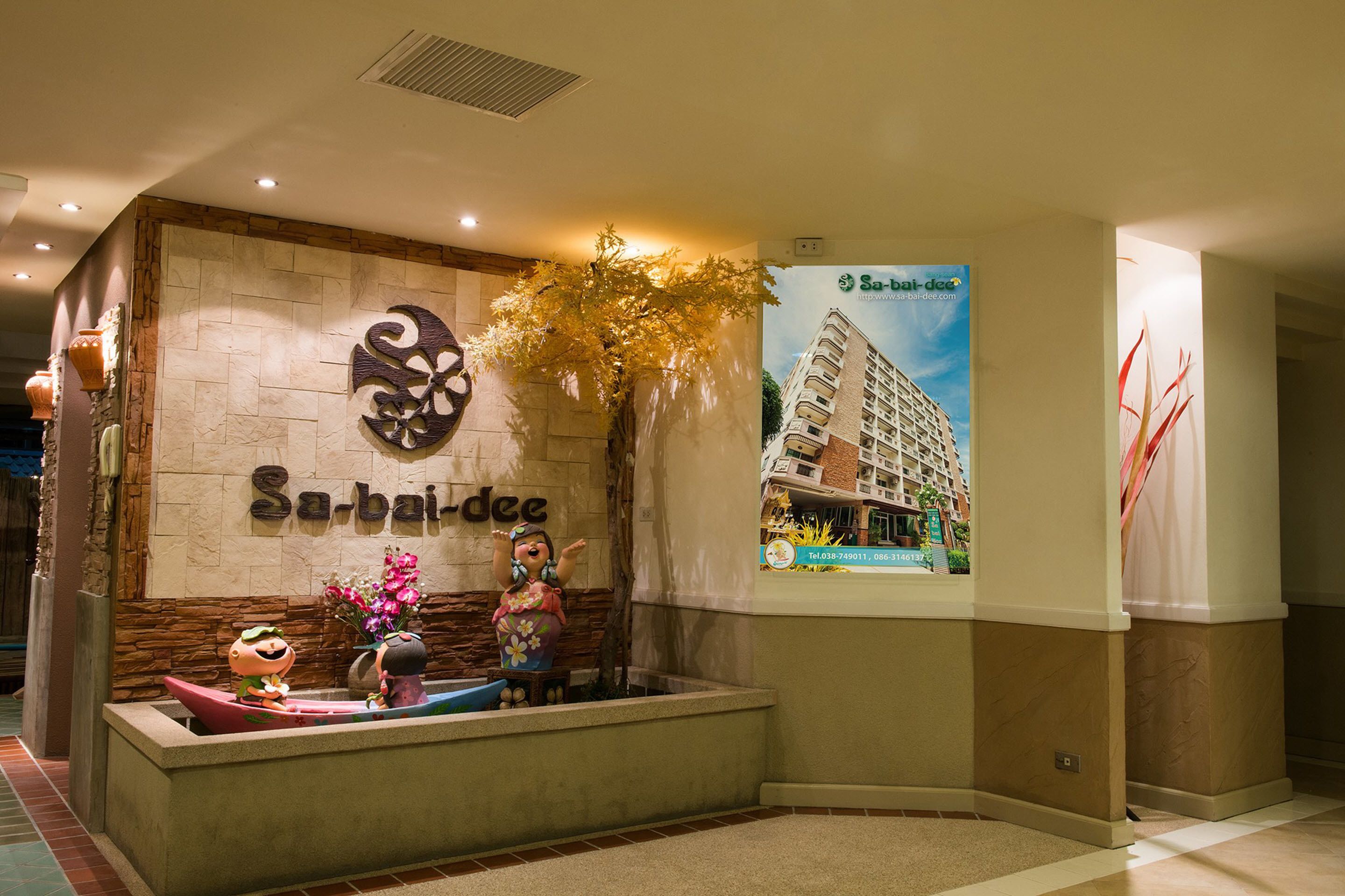 Un área de recepción con pared de piedra, un logotipo, un cartel de un edificio y un mostrador de recepción con una estatua y flores.