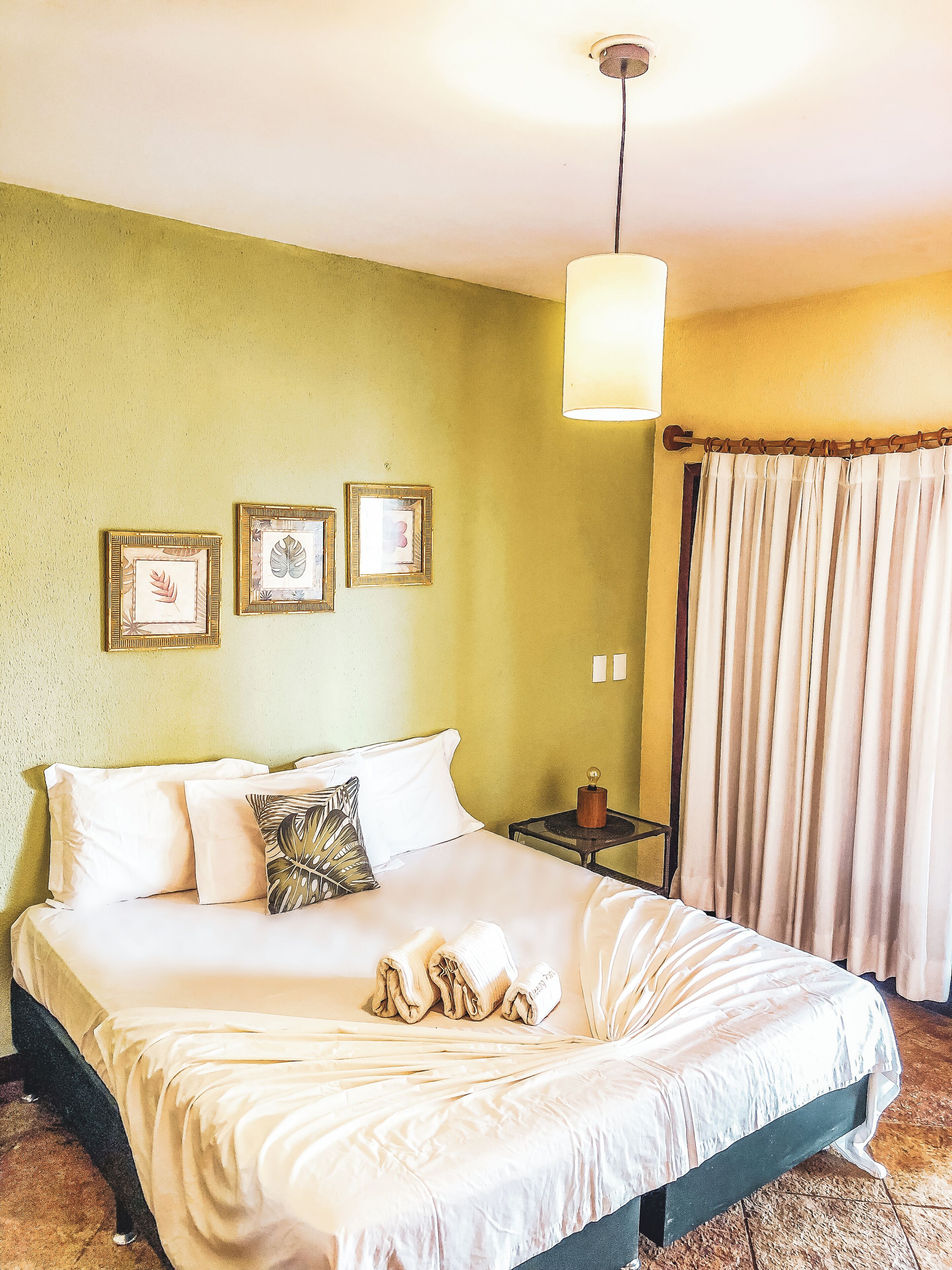 Un letto rifatto con lenzuola bianche, un comodino con una lampada e tre quadri appesi al muro.
