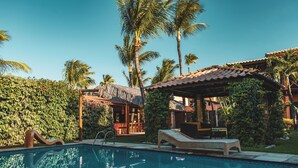 A pool area with lounge chairs, a thatched-roof structure, and palm trees. - Pousada Cumbuco Meeting Point (Caucaia)