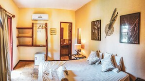 A hotel room with a bed, a bedside table, a mirror, a wall-mounted air conditioner, a framed artwork, and a 'Smile More' sign. - Pousada Cumbuco Meeting Point (Caucaia)