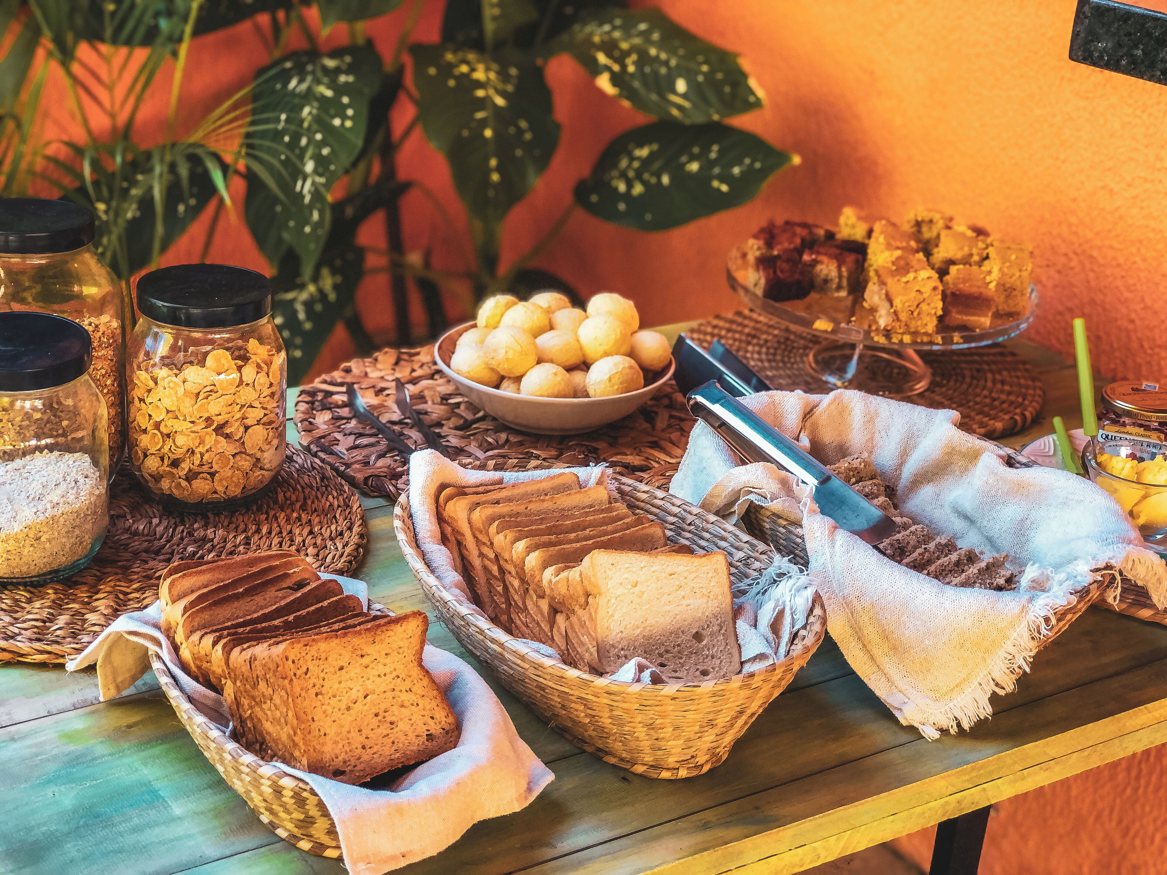 Una mesa con diversos alimentos, como pan, frascos con cereales y un bol de productos de pastelería.