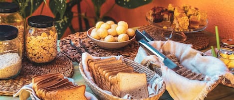 Una mesa con diversos alimentos, como pan, frascos con cereales y un bol de productos de pastelería.