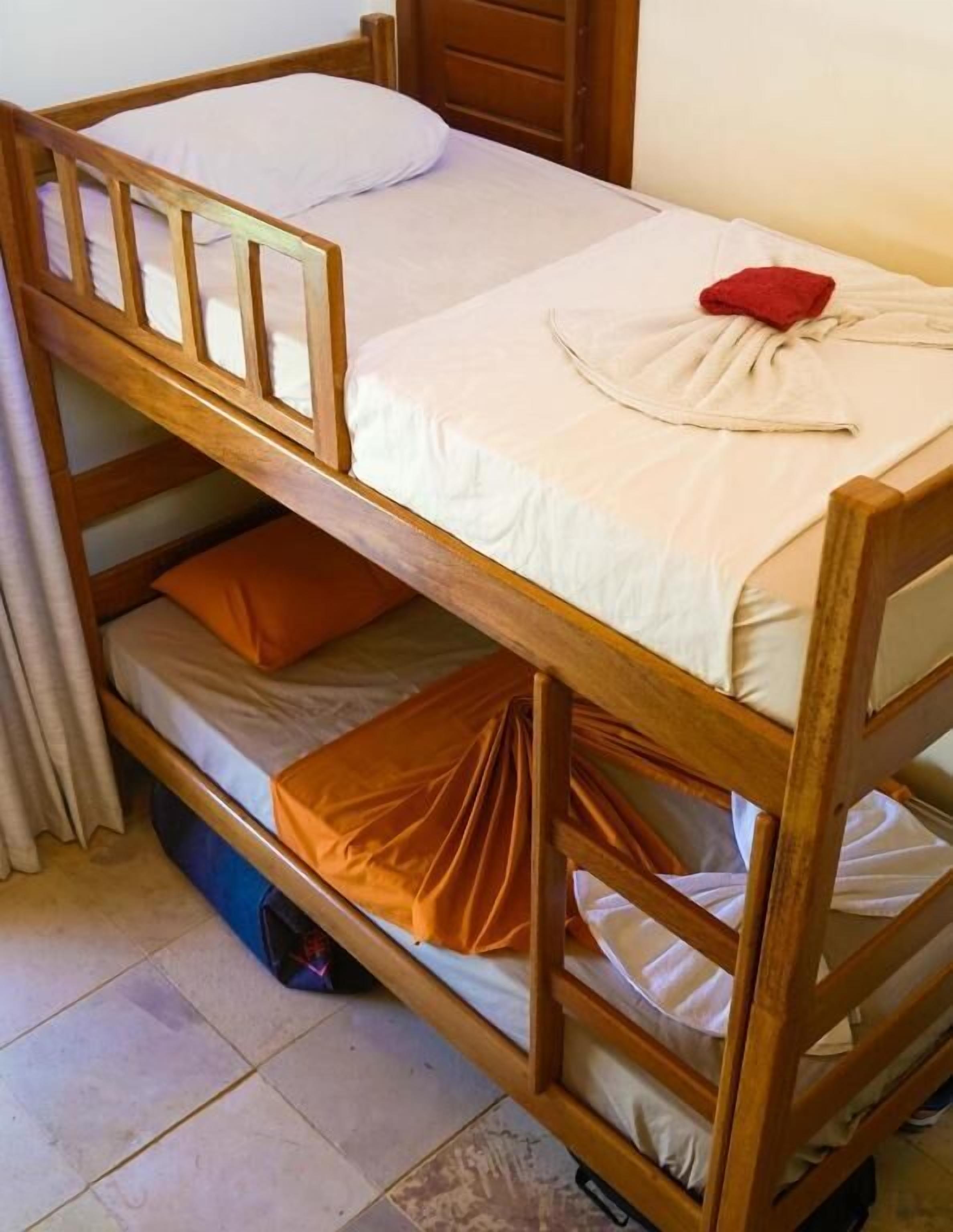A bunk bed with a wooden frame, white bedding, and a red towel.