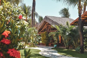 A thatched-roof structure surrounded by lush greenery and palm trees. - Pousada Cumbuco Meeting Point (Caucaia)