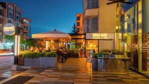 Un restaurante con terraza, un cartel y contenedores de reciclaje.