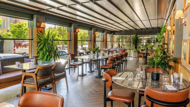 Un restaurante con mesas, sillas y plantas en macetas, con espacio interior.