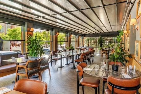A restaurant with indoor seating, large windows, and potted plants.. Alan Suites