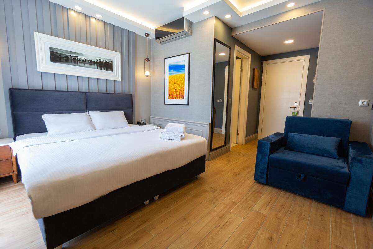 A modern bedroom with a large bed, a blue armchair, wooden flooring, and a framed picture on the wall.