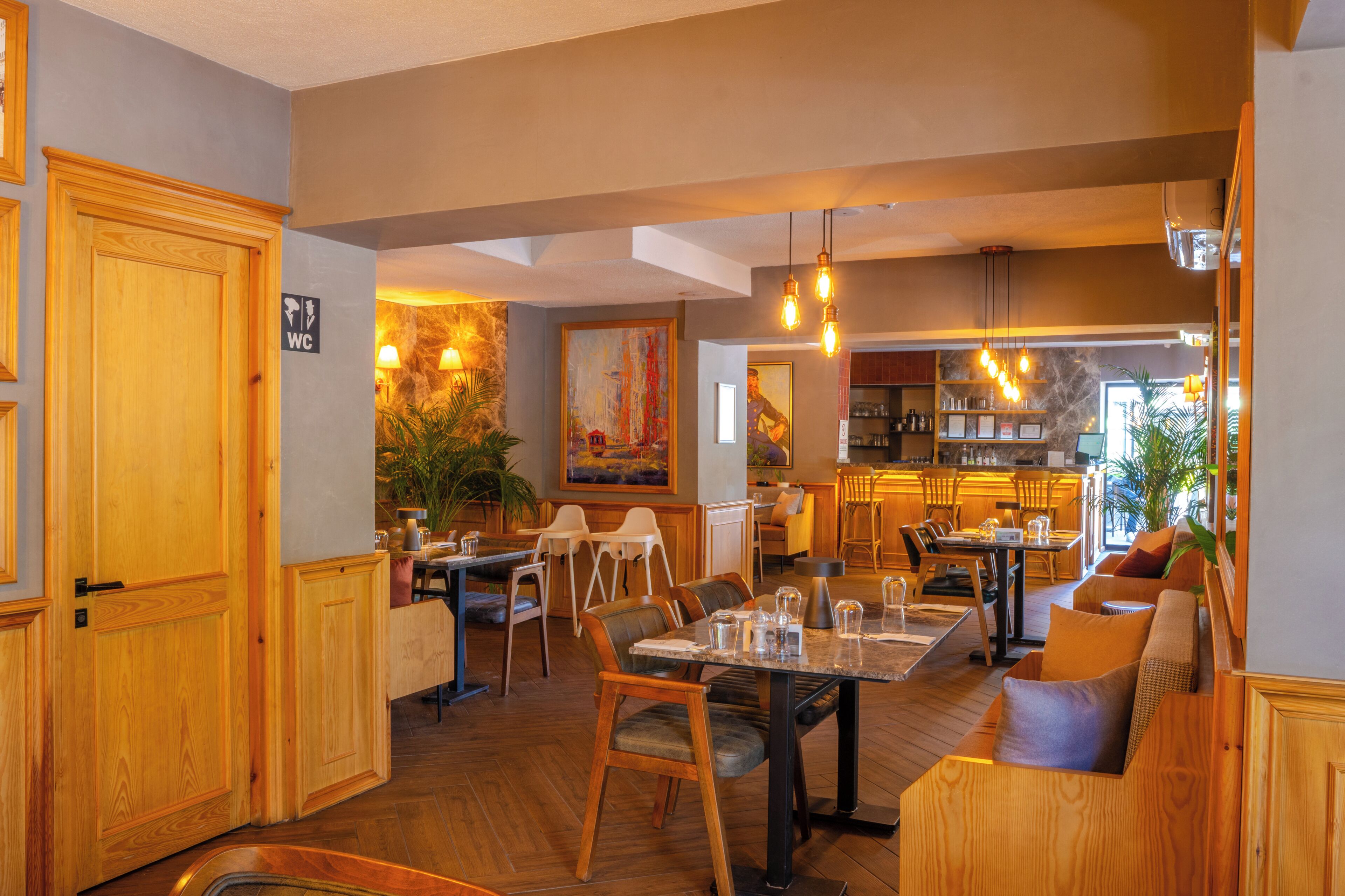 A restaurant with wooden furniture, a bar area, and a painting on the wall.
