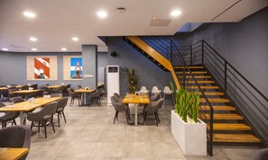 Un restaurant moderne doté de plusieurs tables et chaises, d’un escalier et d’une grande plante.