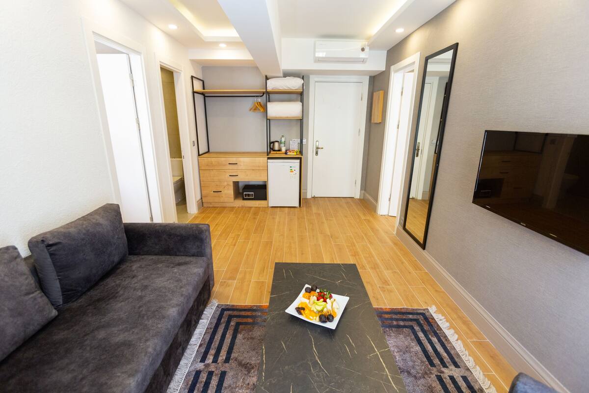 A compact living space with a sofa, a dining table with a plate of food, a kitchen area, and a TV mounted on the wall.