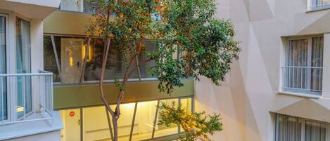 Un edificio moderno con fachada de vidrio, un pequeño árbol en el patio y una puerta visible con un cartel.
